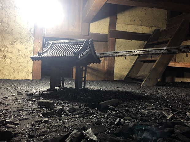 「町蔵」岩崎貴宏：蔵の中に積み上げられたたんすや、家具などで作られた細い通路をくぐり土間から一段上がると、炭の黒色で覆われた地平が現れ、空襲を受けた戦後の名古屋の風景を想起させる。