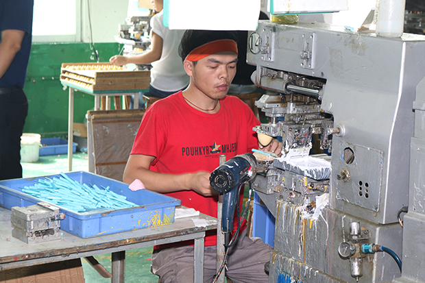 タンポ印刷の機械を操る工員。一つ一つ、目視で確認。